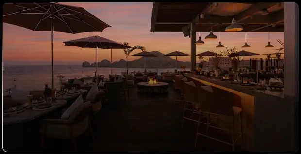 Terraza de restaurante frente al mar de Los Cabos al atardecer con sombrillas y fogata