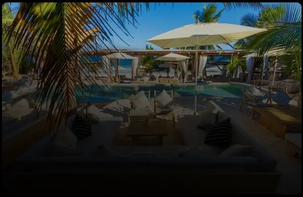 Piscina rodeada de palmeras y sombrillas en Grupos Tulum