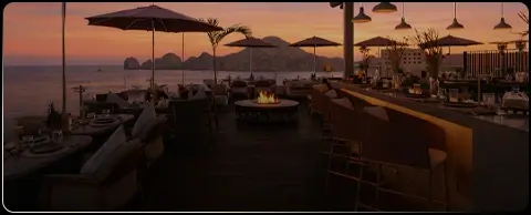 Seafront restaurant terrace in Cabo at sunset, with umbrellas and a fire pit